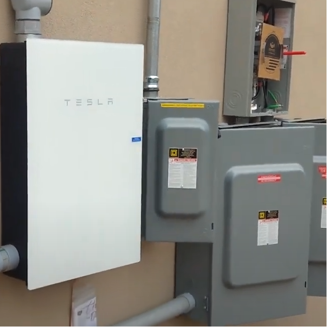 Tesla battery system installed on a wall with electrical panels.